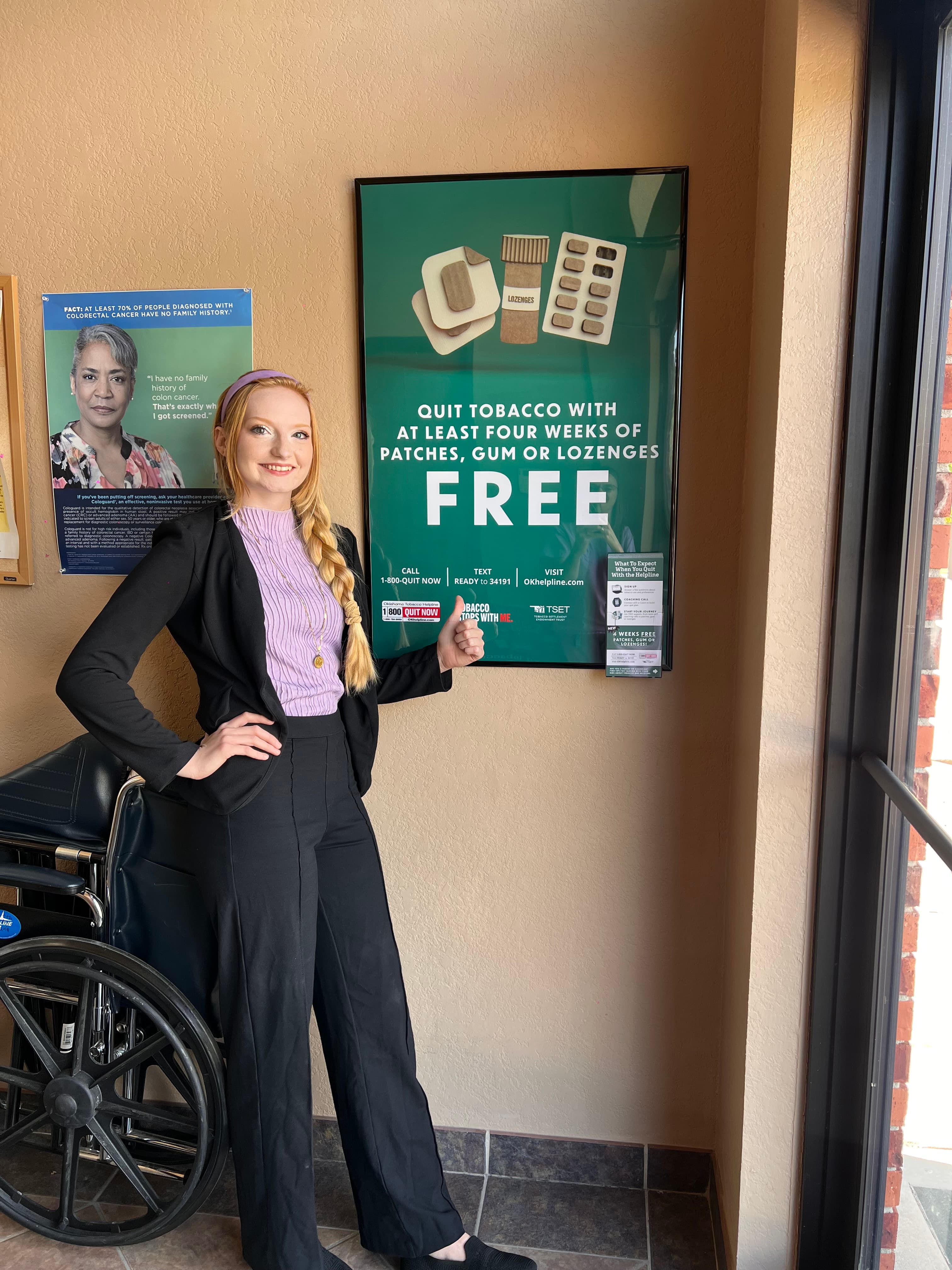 A team member giving a thumbs up beside quit-tobacco posters and take-one materials displayed in a family medicine office