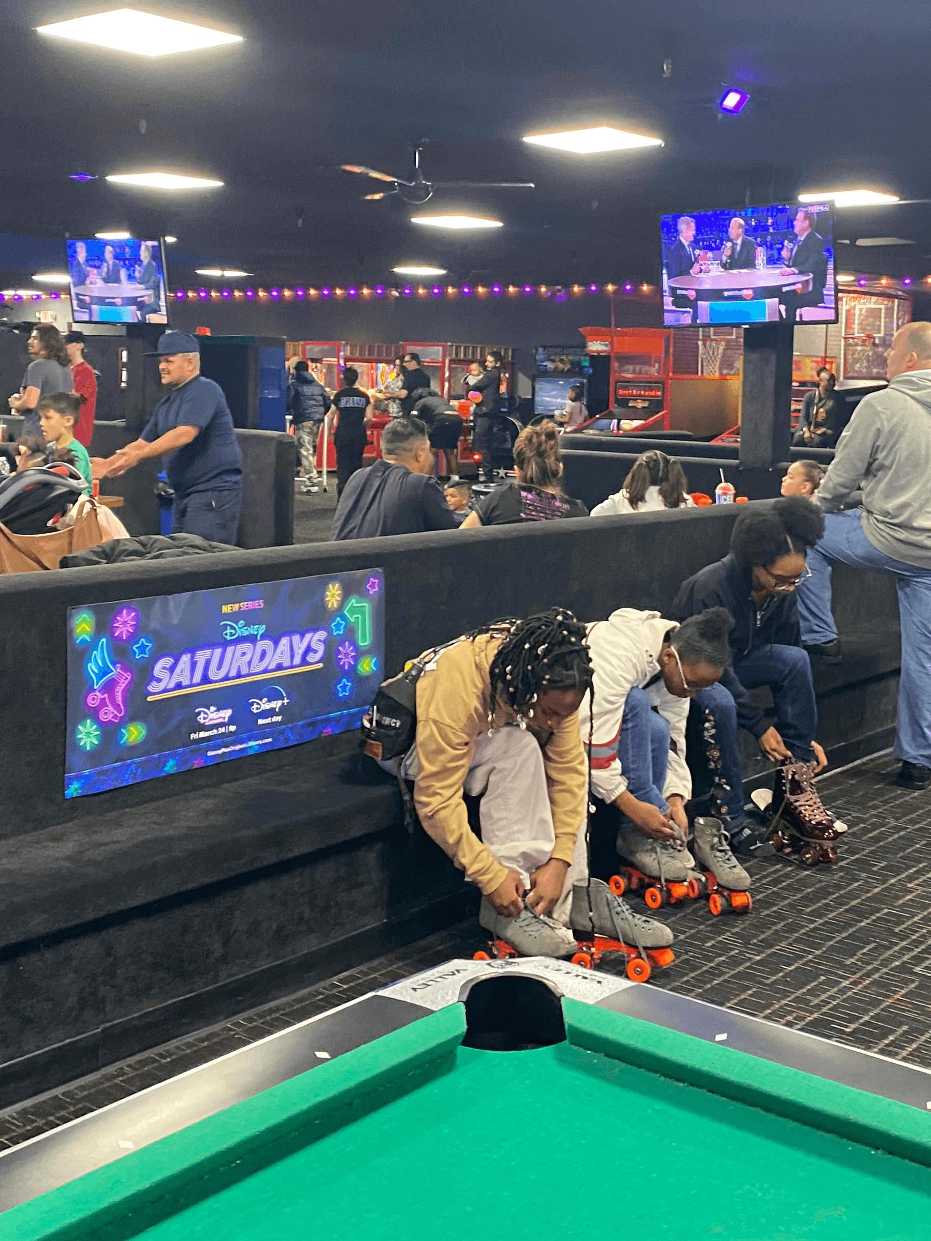 Families lacing up skates beside a colorful campaign bench decal at a roller rink